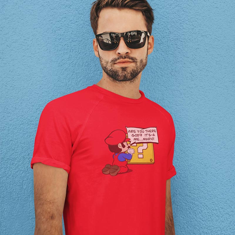 A man wearing a red funny gamer tee with a graphic of Mario asking, "Are you there god? It's a me, Mario." by Dodo Tees.