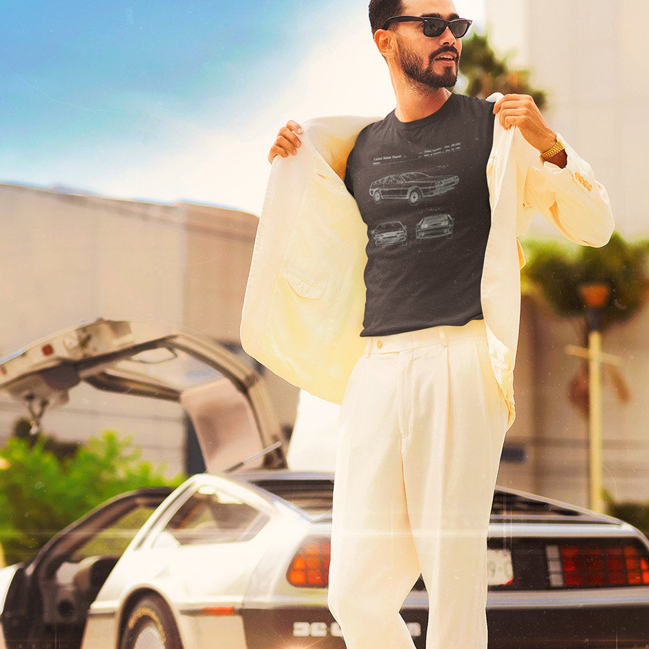 guy standing in front of a DMC 12 car wearing a 80s t shirt featuring the DMC patent drawings. The automotive streetwear is the epitome of a tailored, modern aesthetic.