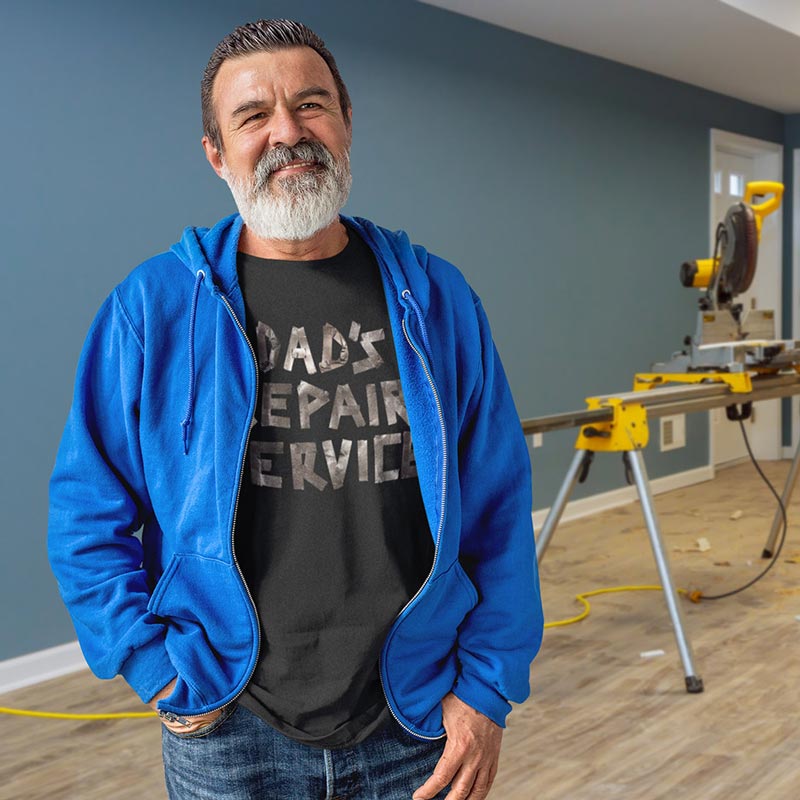 gray haired man by miter saw wearing blue jacket and dads repair service dad joke t shirt