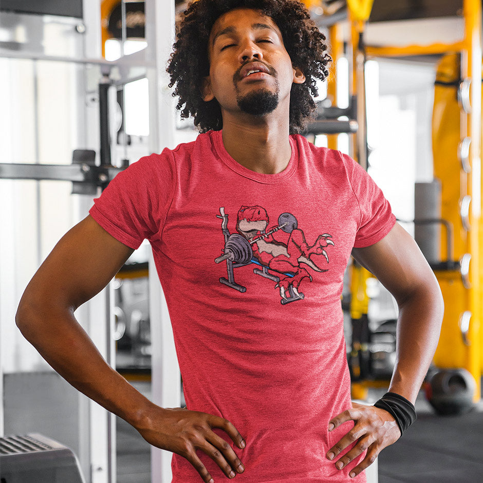 Guy at the gym wearing wearing a funny gym shirt featuring a weight lifting t rex dinosaur. The Funny Workout Shirt is side-seamed for a tailored fit that follows the bodies silhouette.