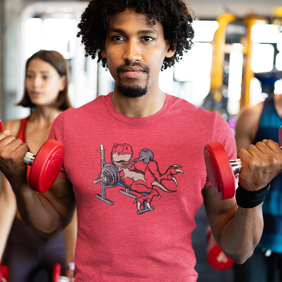 Guy at the gym wearing a funny gym apparel featuring a weight lifting t rex dinosaur. The Gym Shirts For Men are made from buttery soft fabric and side-seamed for a great fit.
