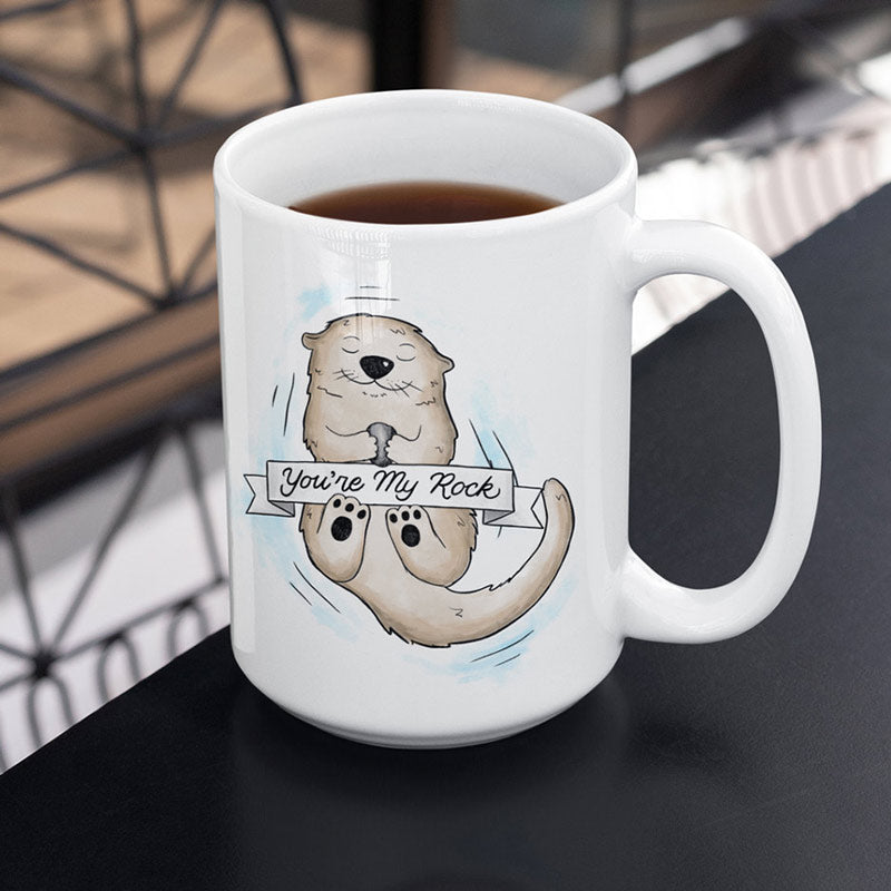 otter mug by dodo tees with illustration of otter floating in water holding rock with banner saying "you're my rock"