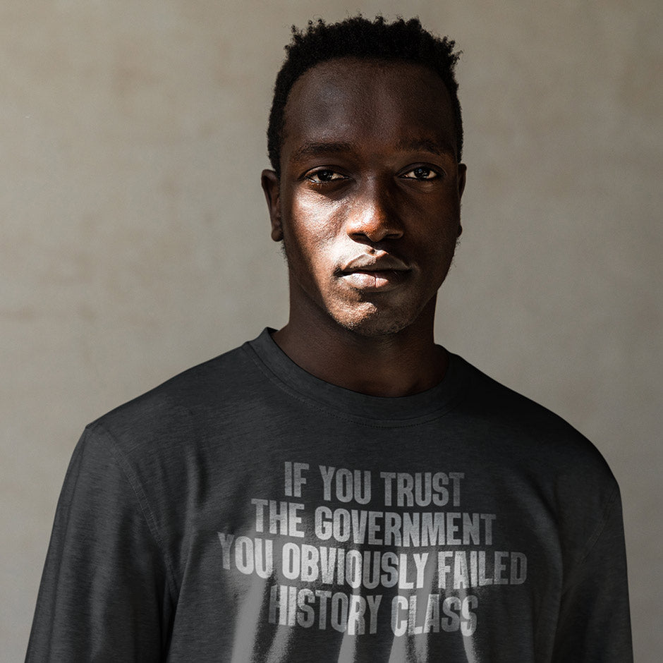 man looking at camera wearing political shirt with if you trust the government you obviously failed history class typography