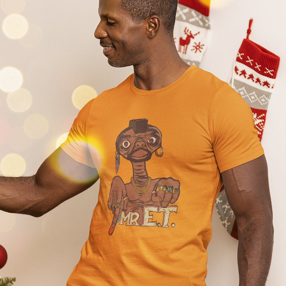 man in front of Christmas stockings wearing a white elephant gift exchange Mr. ET shirt by Dodo Tees. The nerd t shirt features an original illustration of ET dressed up like Mr. T. 