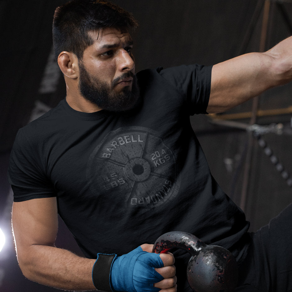 kick boxer wearing a workout shirt featuring a faded barbell. The mens gym apparel features a fades barbell design by Dodo Tees.