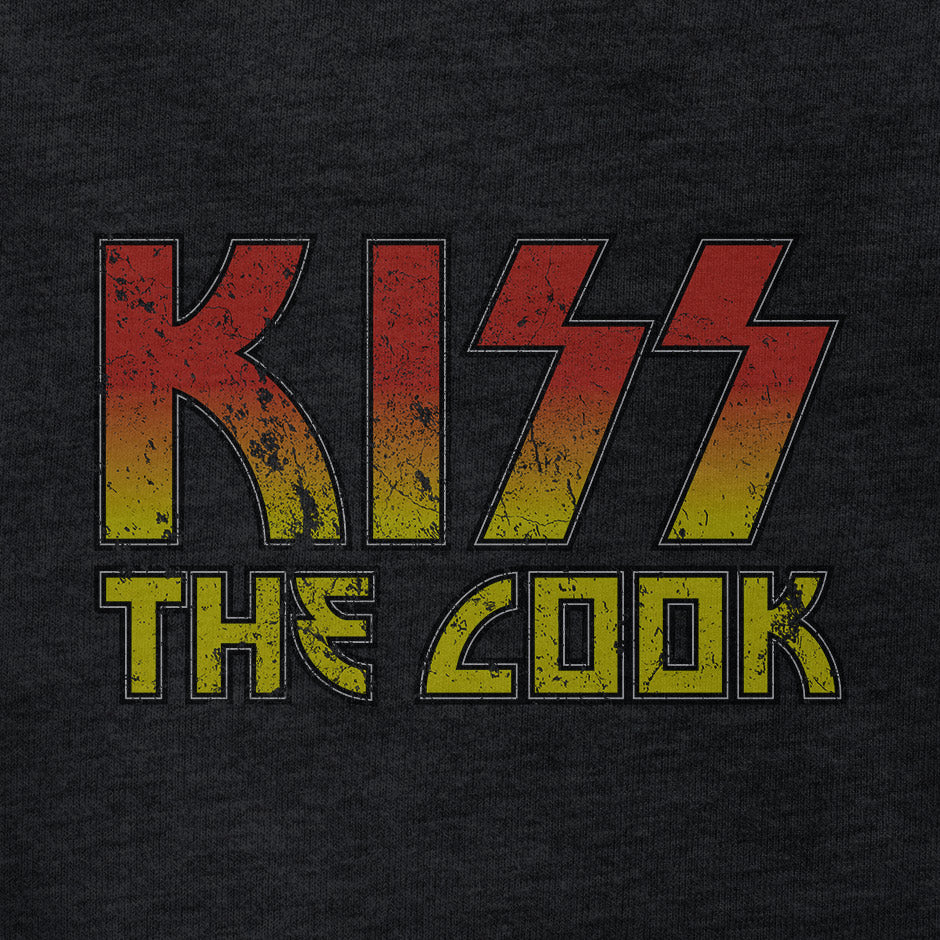 funny t shirt reading kiss the cook. The funny dad shirt features a distressed printing style for that worn in look.