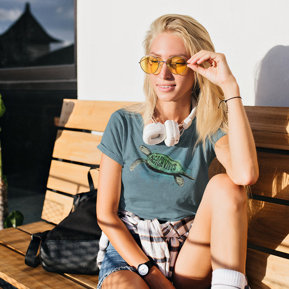 blonde woman on bench wearing surfing t shirt with beach vibes turtle illustration. our beach tee shirts make beautiful gifts for her,