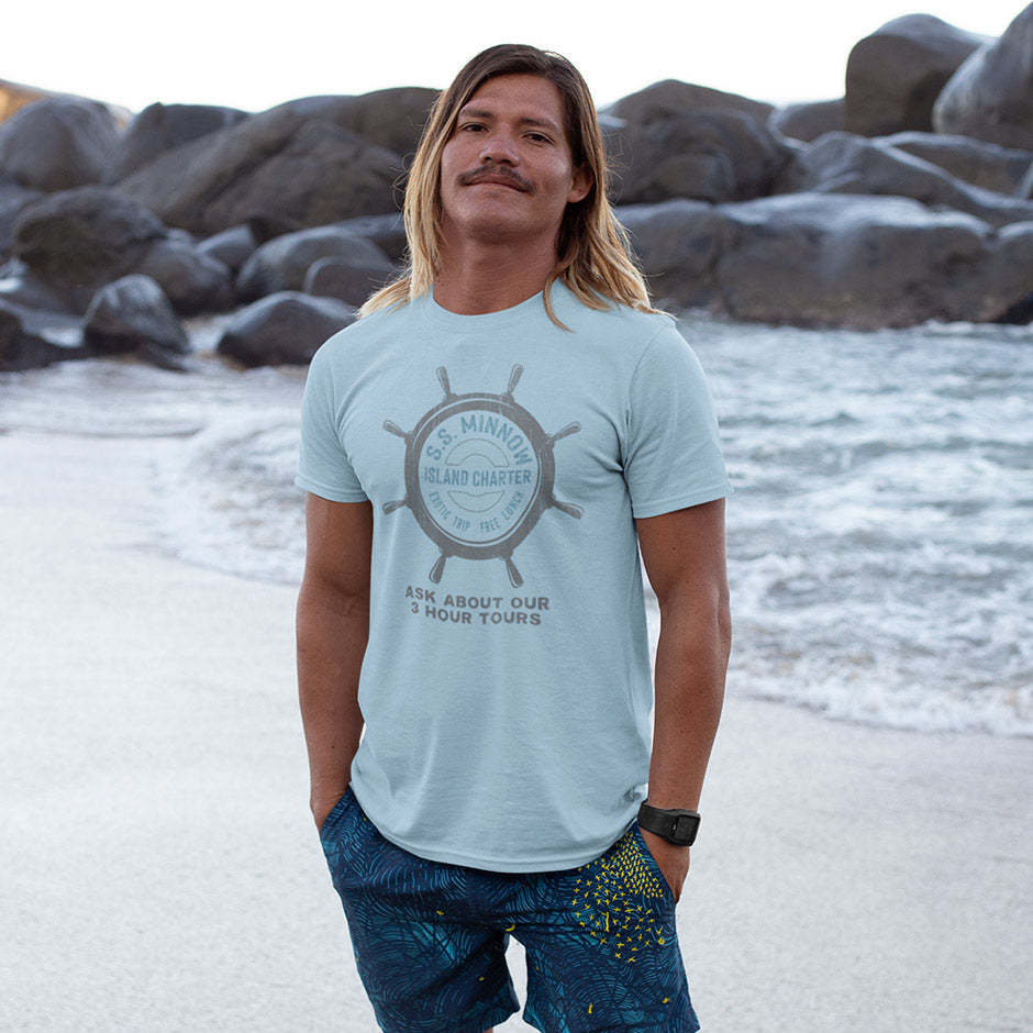 smiling man on beach wearing surfing t shirt with ss minnow logo. The retro 1960s clothing has a lived in look via the distressed printing style.